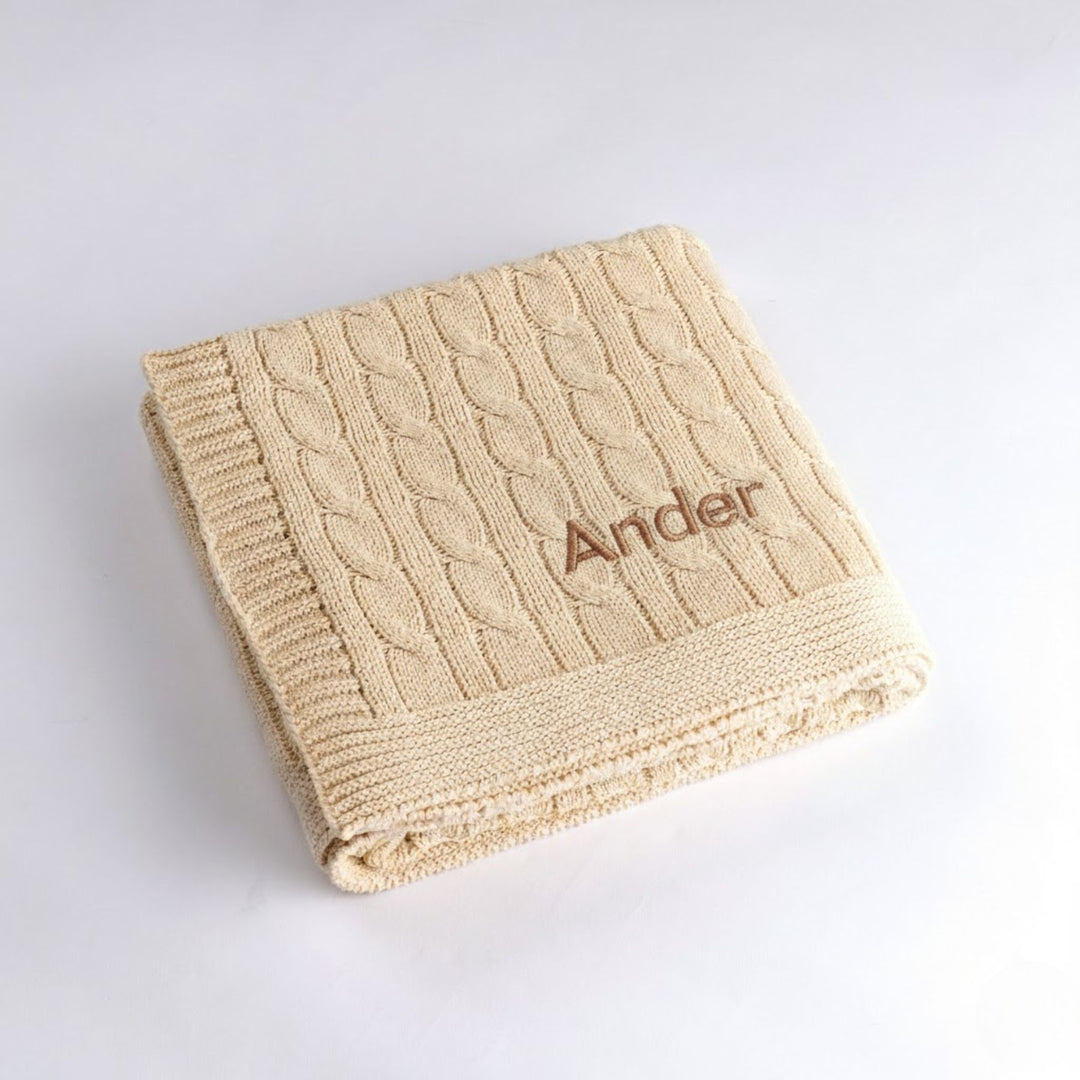 Cream cable knit blanket with 'Ander' embroidery on a light gray background
