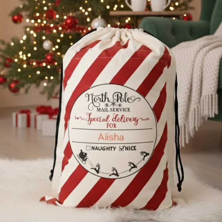 Red and white striped gift bag with personalised label in a festive room with Christmas tree and presents.