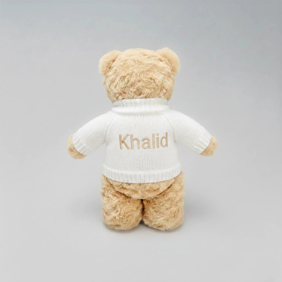 Beige teddy bear wearing a white sweater with 'Khalid' embroidered on a gray background