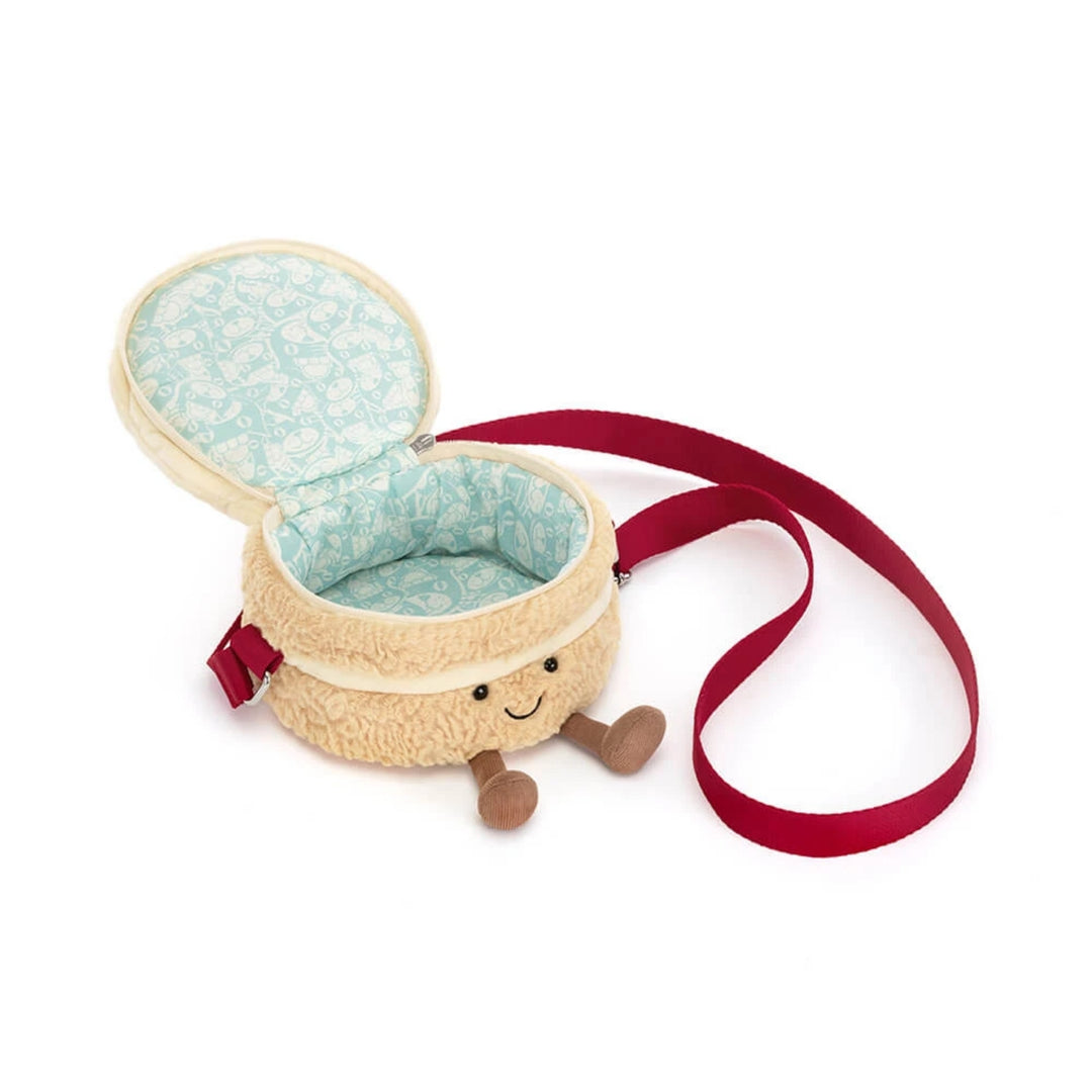 Open birthday cake crossbody bag revealing a light blue patterned fabric lining, zip-top closure, plush cream cake body and red shoulder strap.