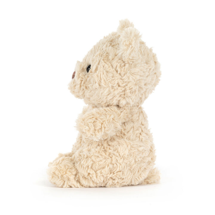Side view of the cream Bartholomew Bear Junior soft toy, showing its rounded head, plush body, small arms and seated shape.