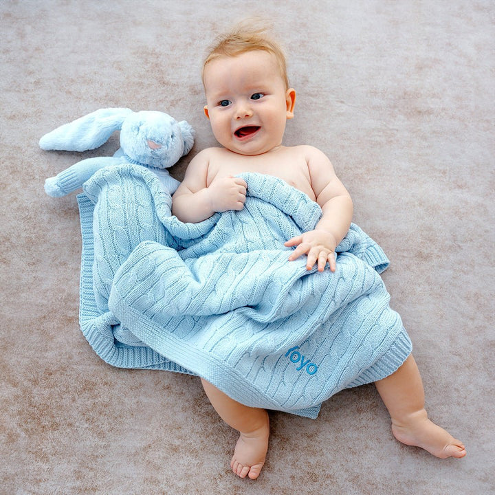 Baby boy and blue jellycat bunny covering with Blue cable knit blanket personalised with "Yoyo" in blue thread