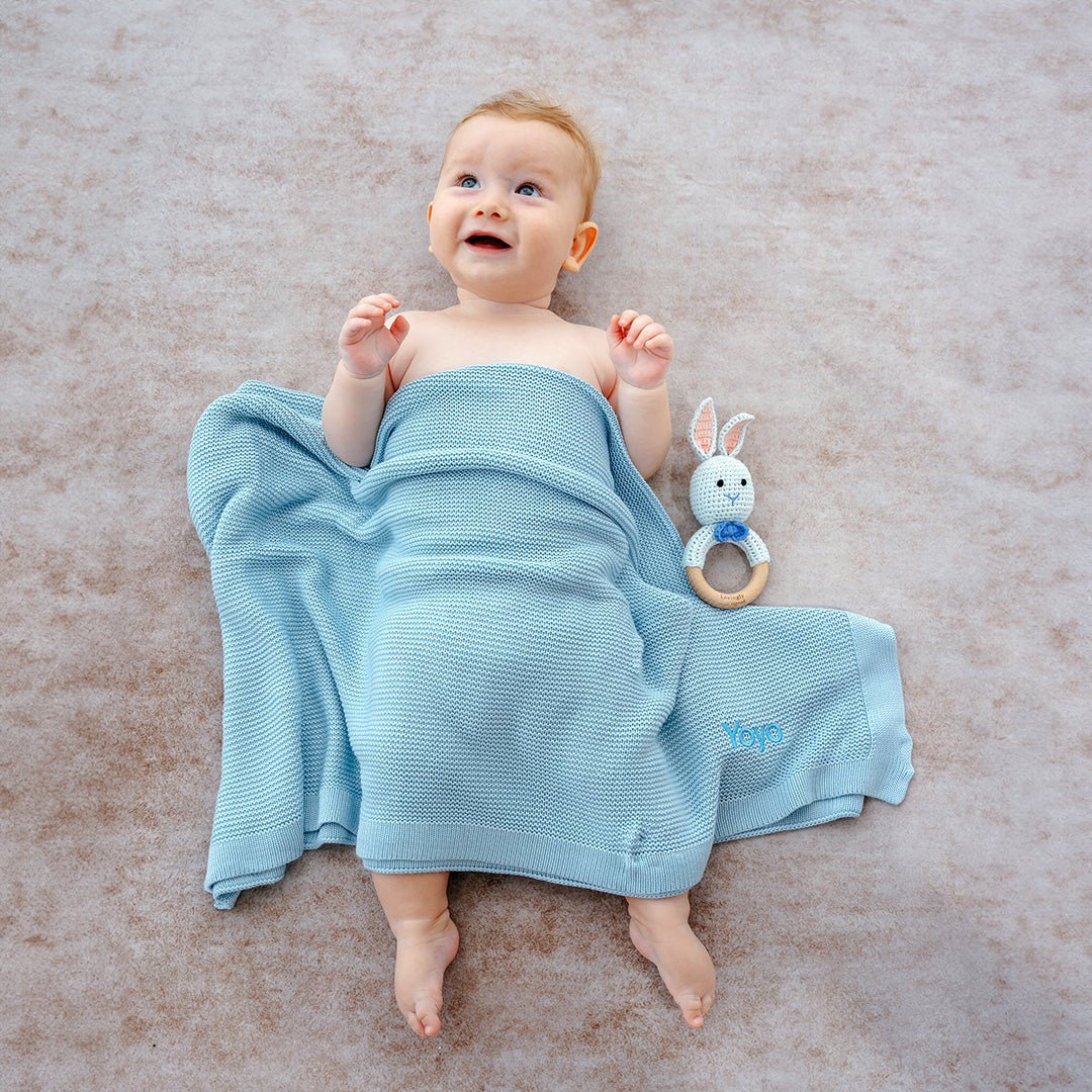 A baby is wrapped in a light blue blanket, lying on a soft surface