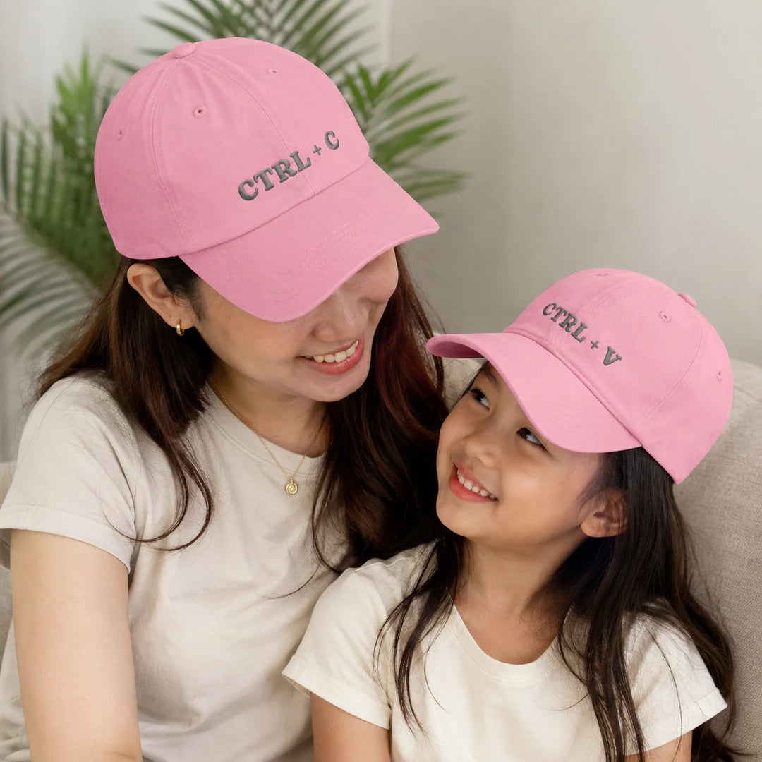 Woman and young girl wearing pink caps with 'CTRL + C' and 'CTRL + V' text, sitting together.