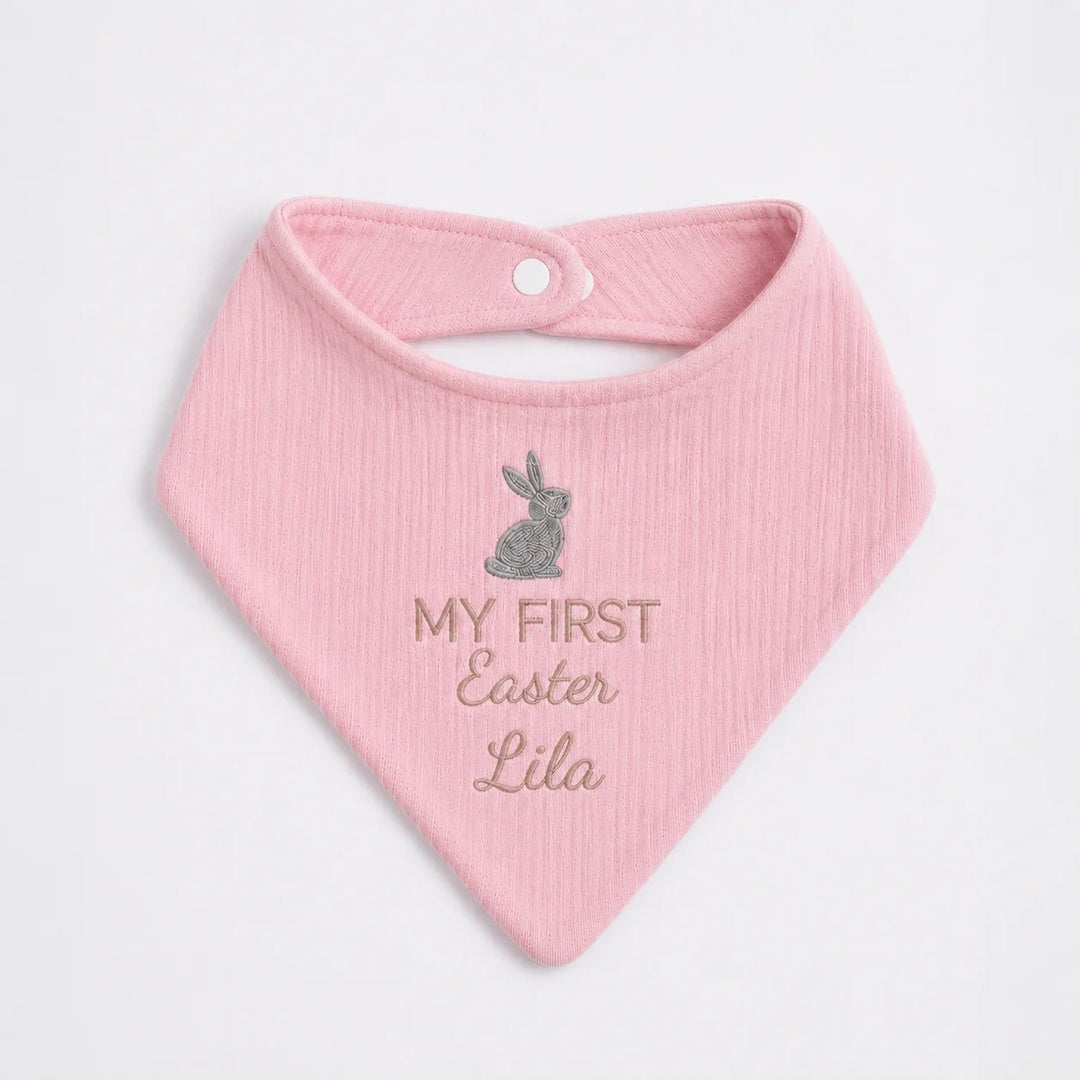Pink baby bib with 'My First Easter Lila' text on a light gray background