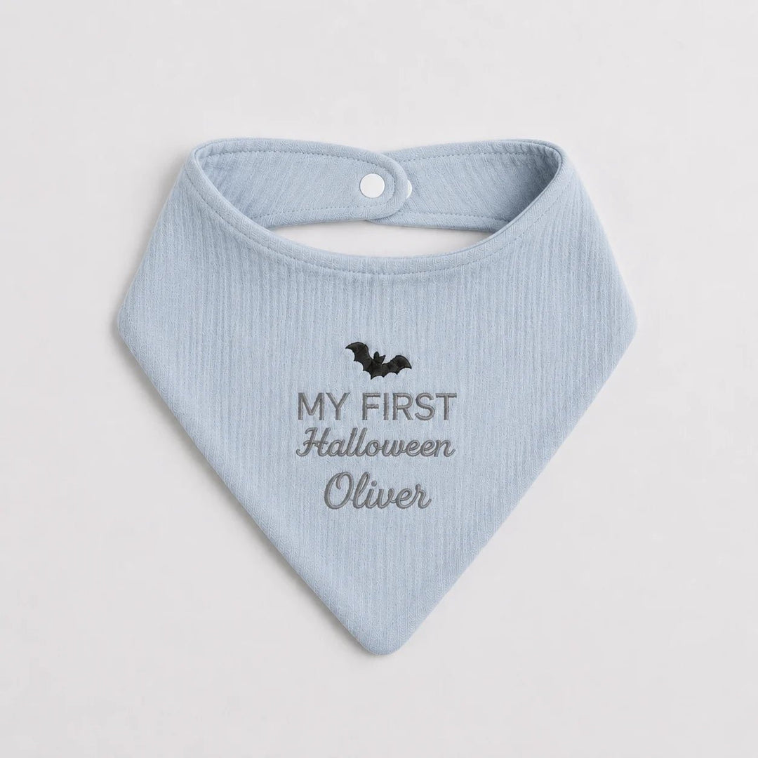 Light blue baby bib with 'My First Halloween Oliver' text and bat design on a light gray background