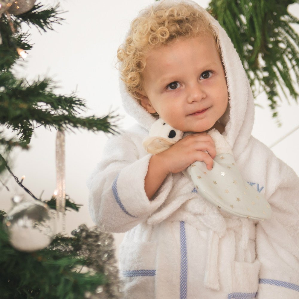 Boy in Blue robe and hugging Jellycat Bashful Polar Bear Stocking 