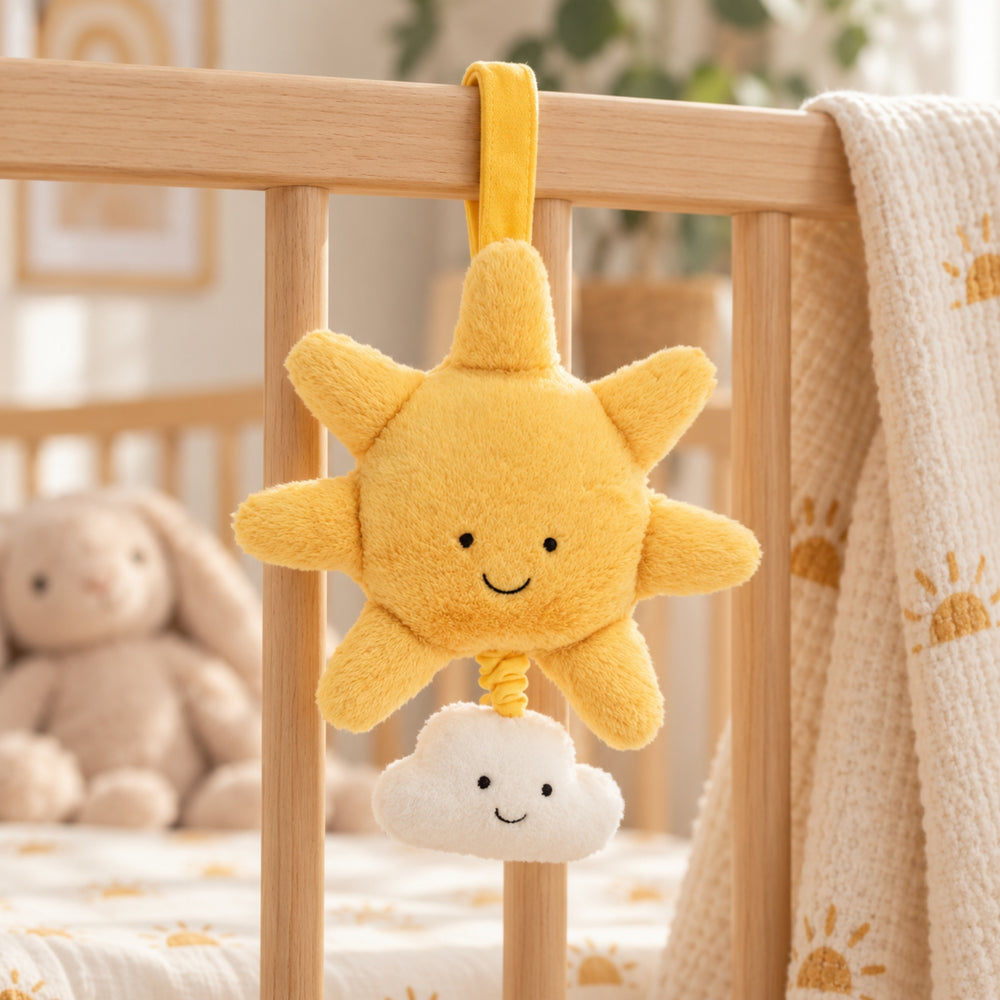 Yellow smiling sun and white cloud musical pull hanging from a wooden cot in a warm neutral nursery, styled with a cream knitted blanket and soft bunny toy in the background.