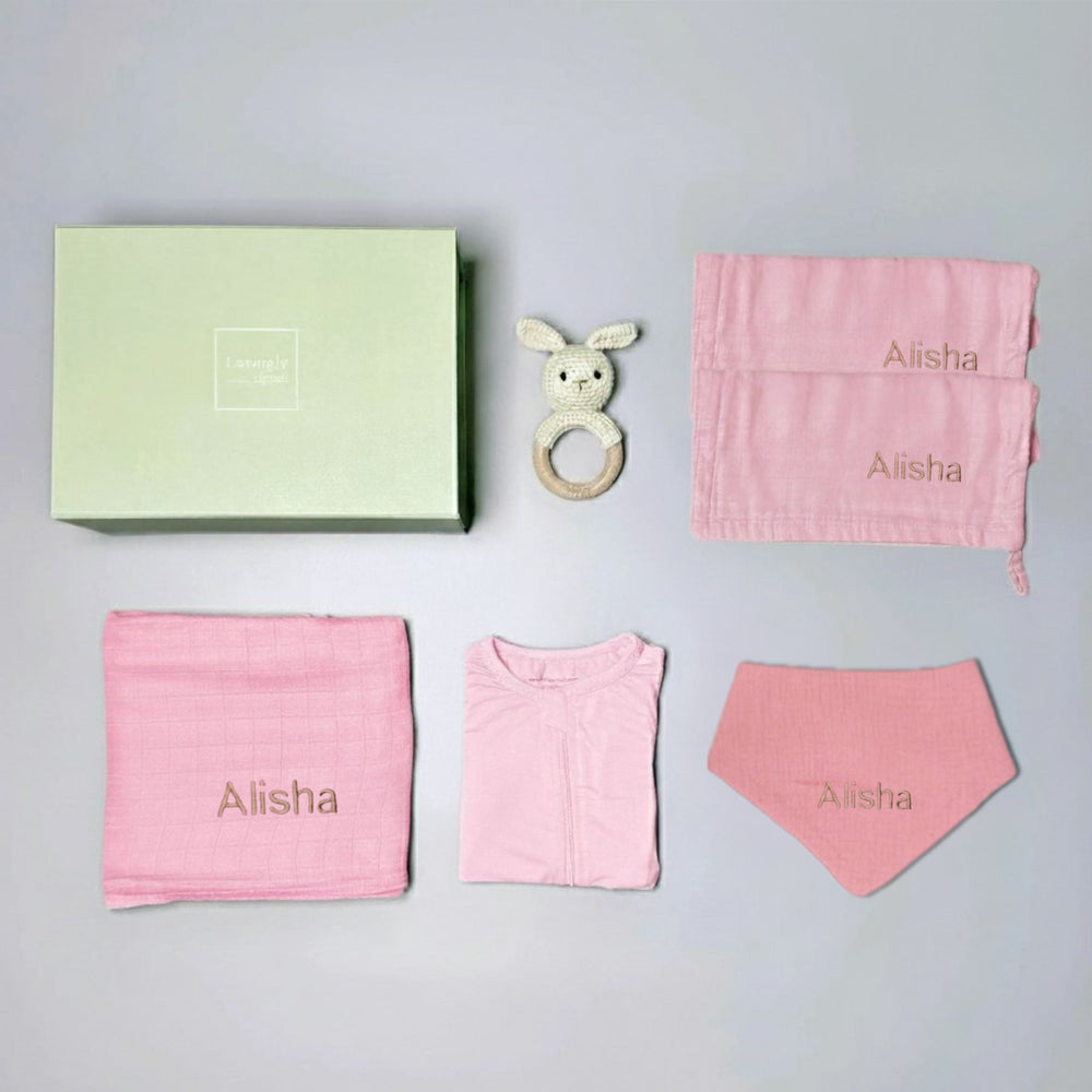 Baby gift set with pink items and a green box on a gray background