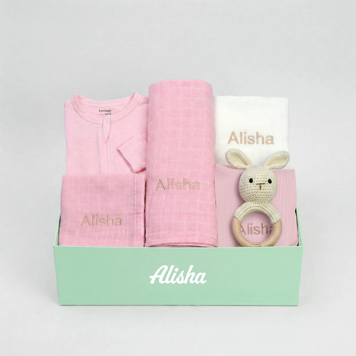 Baby gift set with pink items and a green box on a gray background