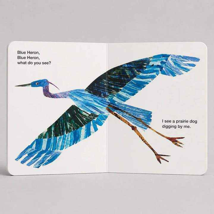 An open children's book spread showing a blue heron illustration with printed text on both pages, photographed against a light gray background.