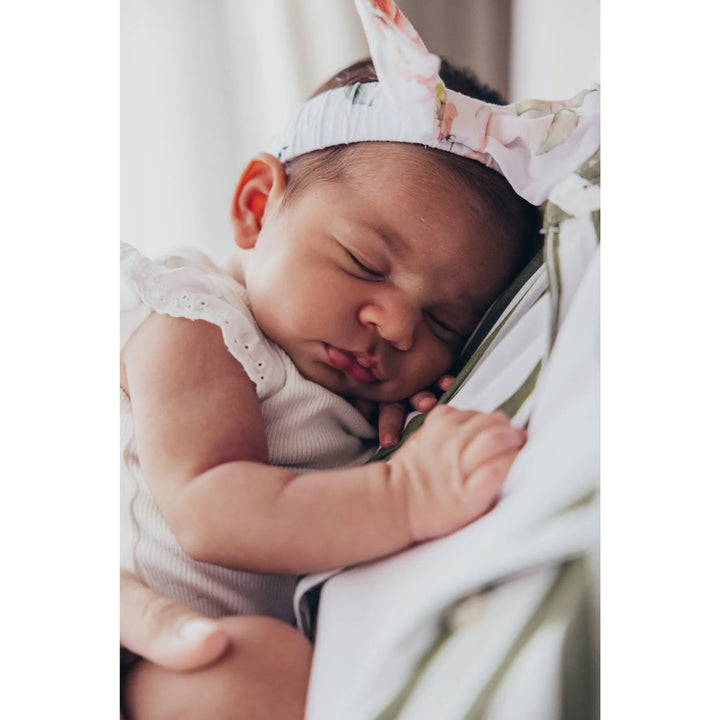 Newborn baby sleeping peacefully in a sling with a floral headband, photographed by Katie Martin-Sperry Photography