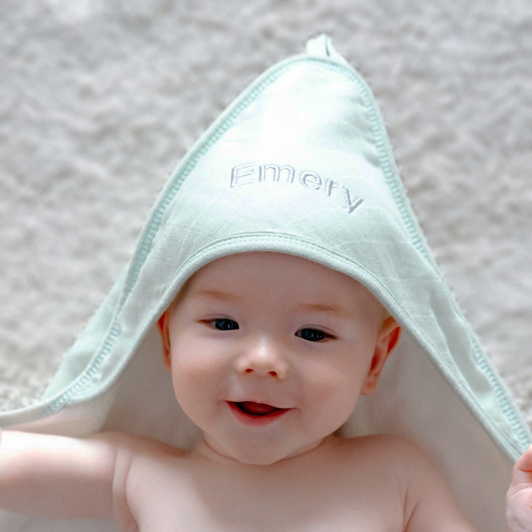 Baby wearing Green Bamboo Hooded Towel Personalised with "Emery" in Grey Thread