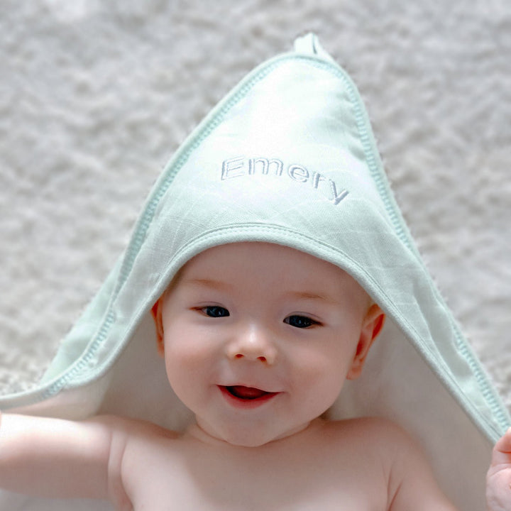 Baby wearing Green Bamboo Hooded Towel Personalised with "Emery" in Grey Thread