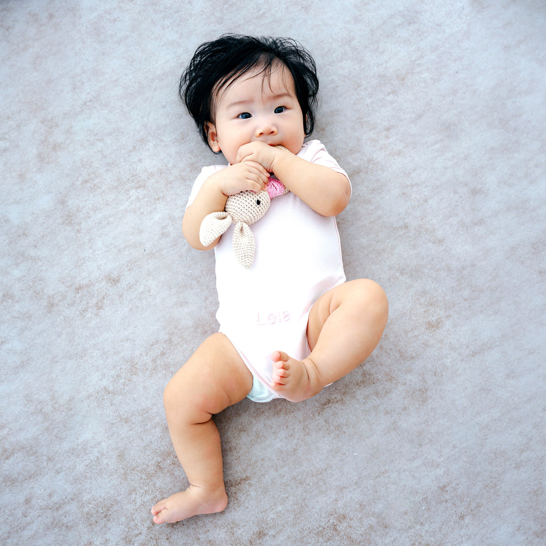 baby in Pink Short Sleeve Babygrow playing with teether