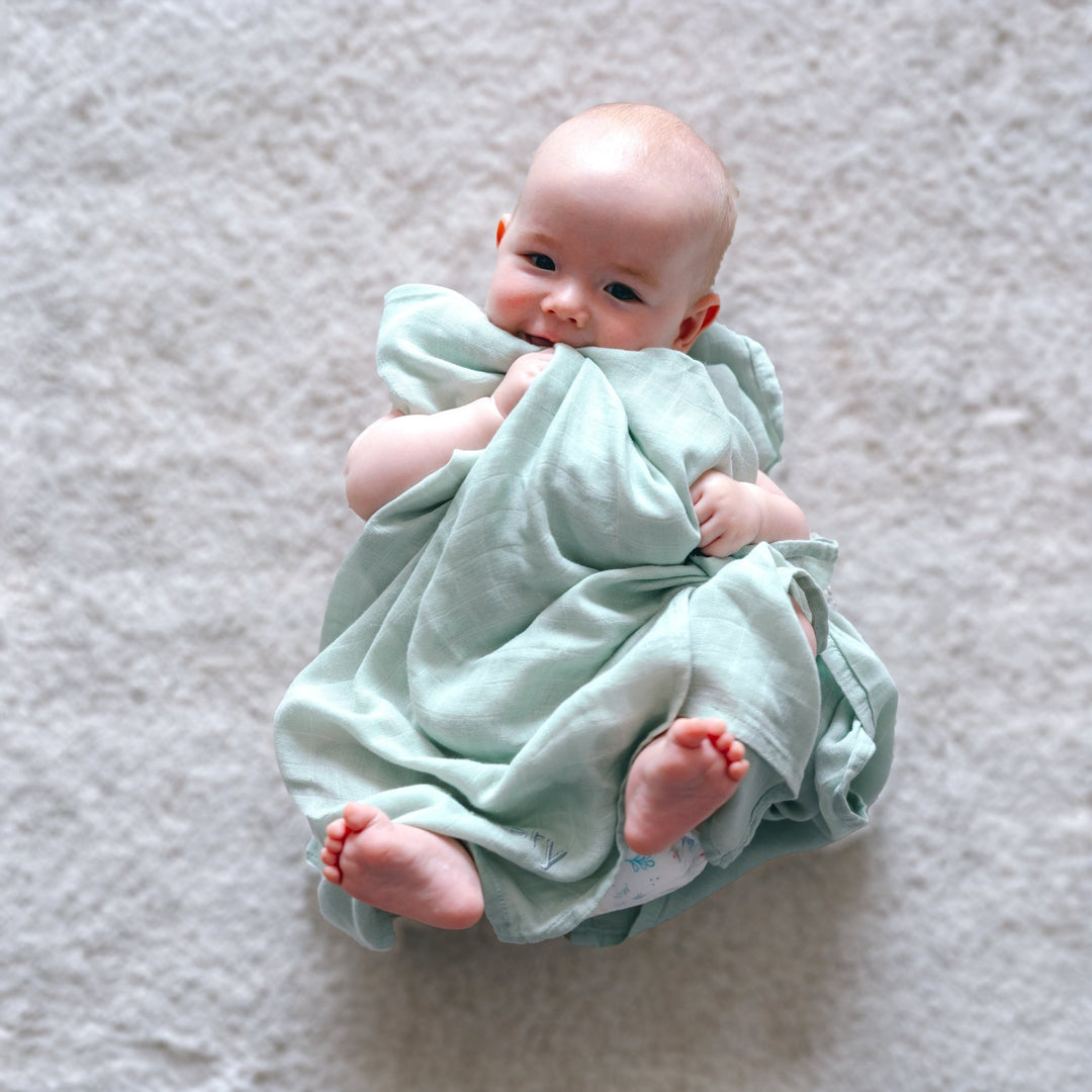 A baby is wrapped in a soft green bamboo swaddle