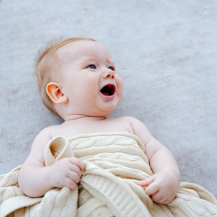 Baby using Cream cable knit blanket 
