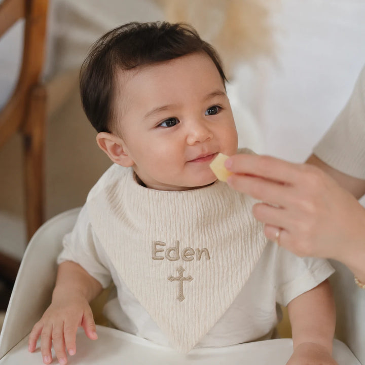 Baby wearing personalised Christian bib with embroidered name Eden and cross
