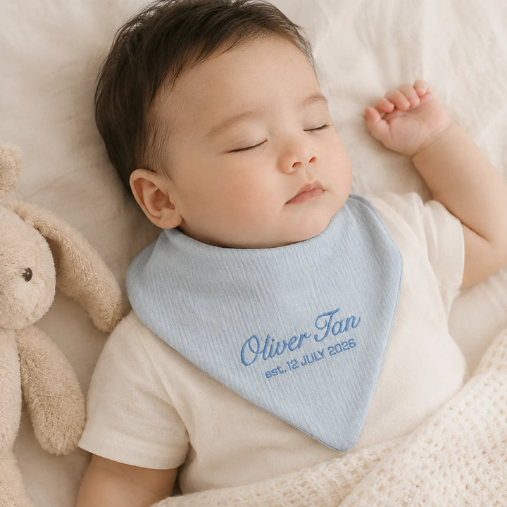 Sleeping baby wearing personalised blue bib with embroidered name Oliver Tan and birth date