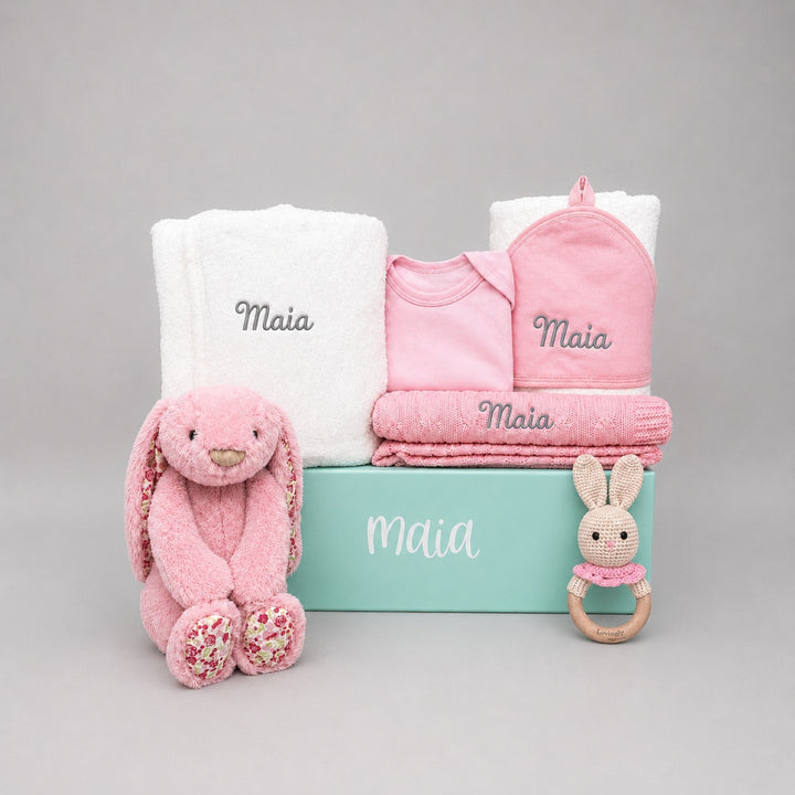 Baby gift set with pink plush toy, baby clothes, and teether on a gray background
