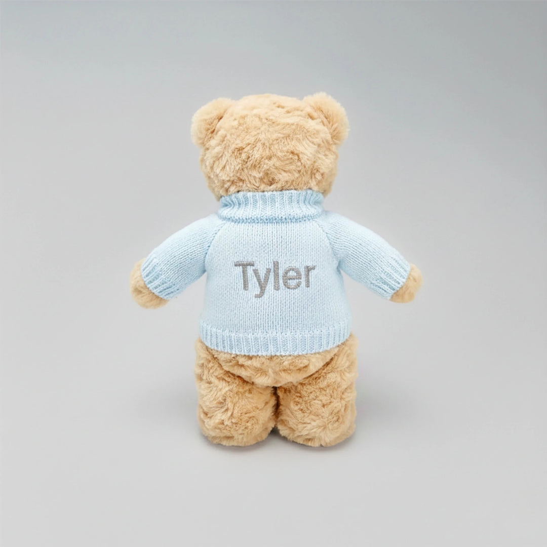 Teddy bear wearing a light blue sweater with 'Tyler' embroidered on it against a gray background