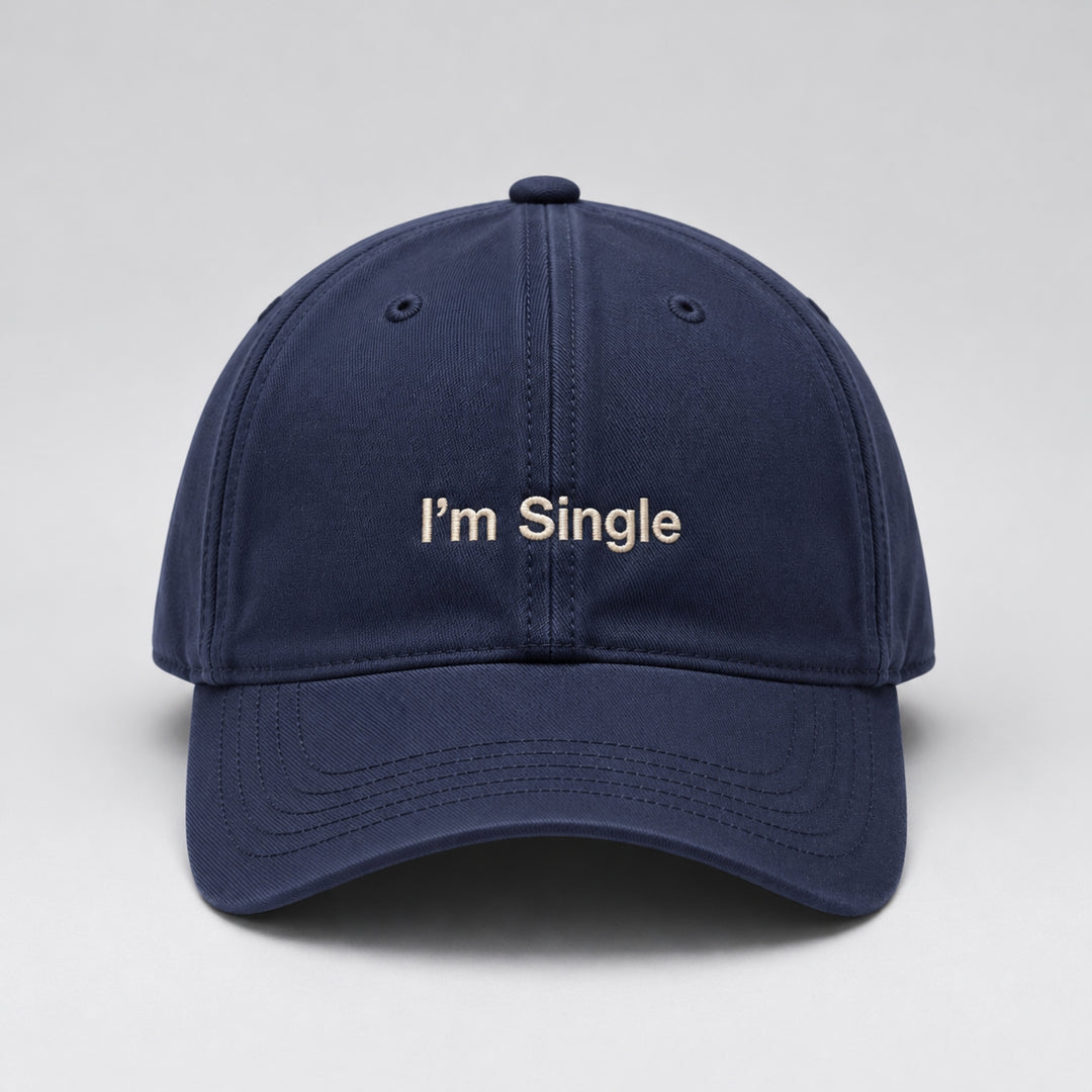 Navy blue baseball cap featuring “I'm Single” embroidered in cream block lettering, with a curved brim and classic six-panel design against a light grey studio background