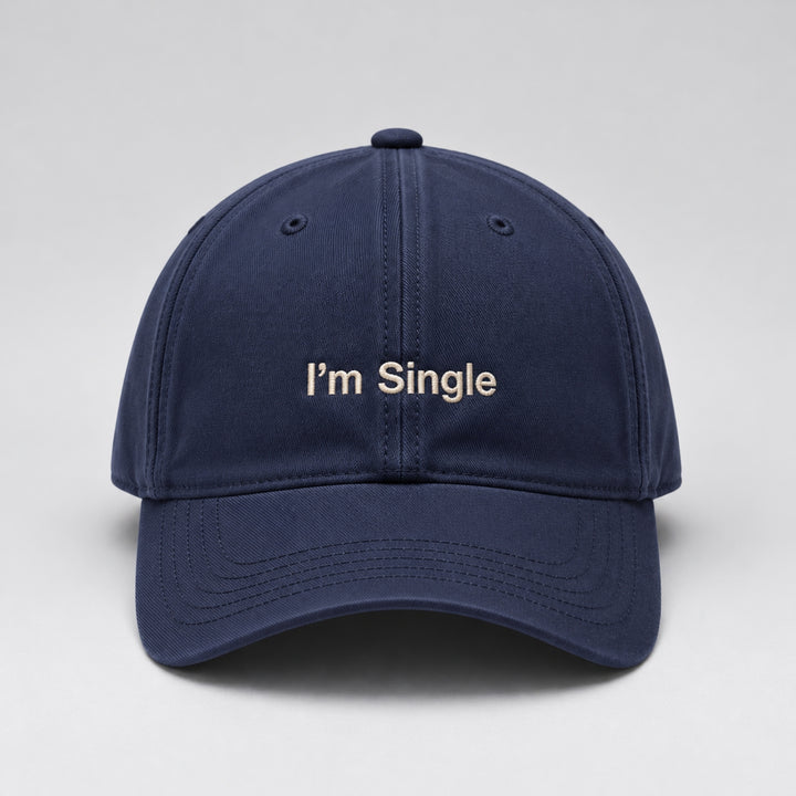 Navy blue baseball cap featuring “I'm Single” embroidered in cream block lettering, with a curved brim and classic six-panel design against a light grey studio background