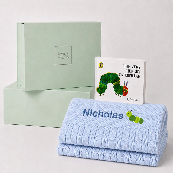 A personalized baby gift set featuring a light blue cable-knit blanket with the name 'Nicholas' and a caterpillar design, a children's book of 'The Very Hungry Caterpillar' by Roald Doolittle, and mint green gift boxes by Lovingly Styled.