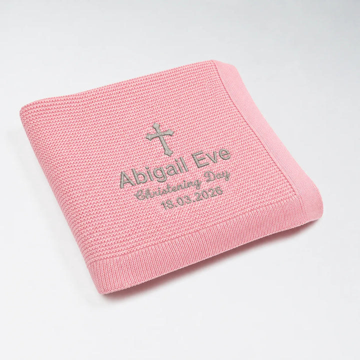 Pink knitted blanket with embroidered text and cross on a white background