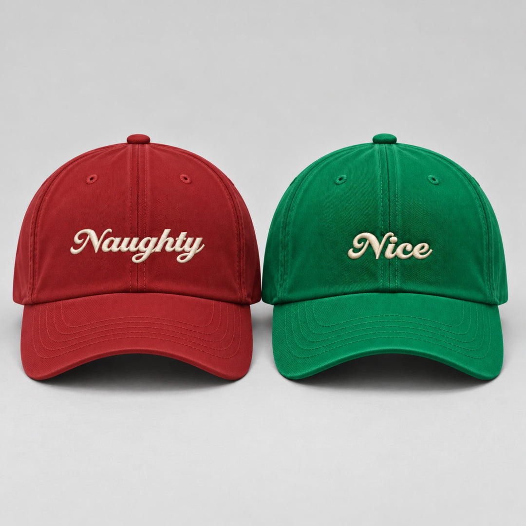 Red “Naughty” and green “Nice” Christmas baseball caps displayed side by side, featuring cream embroidered lettering.