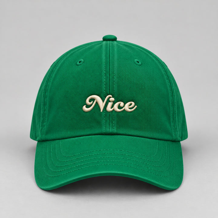 Close-up front view of a vibrant green Christmas baseball cap featuring “Nice” embroidered in cream cursive lettering.