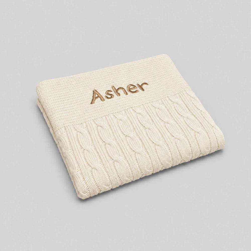 Cream cable knit blanket with 'Ander' embroidery on a light gray background