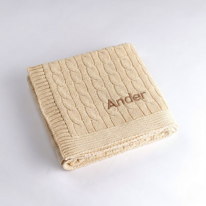 Cream cable knit blanket with 'Ander' embroidery on a light gray background