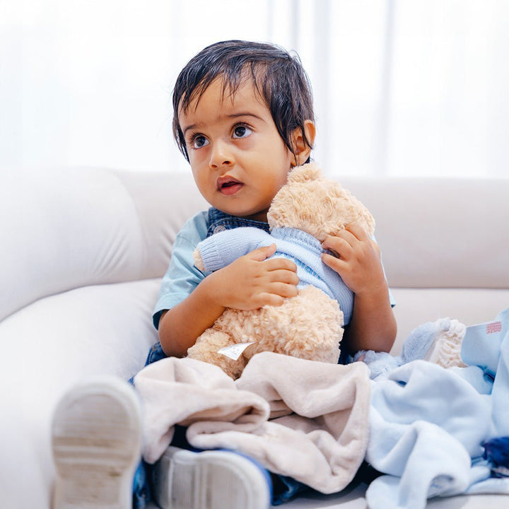 Toddler hugging teddy bear in blue jumper