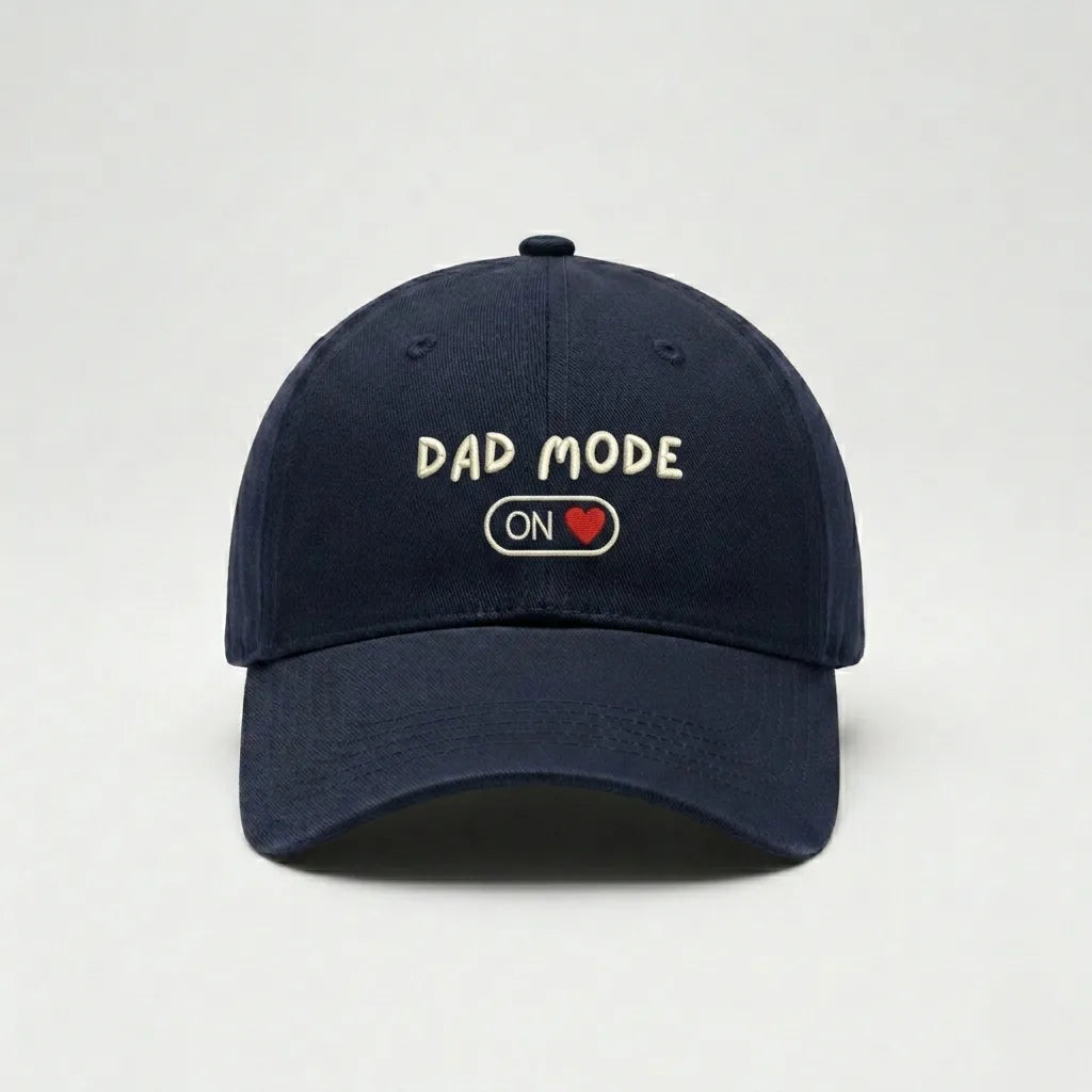 Navy blue cap with 'Dad Mode On' text on a light gray background