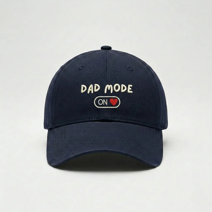 Navy blue cap with 'Dad Mode On' text on a light gray background