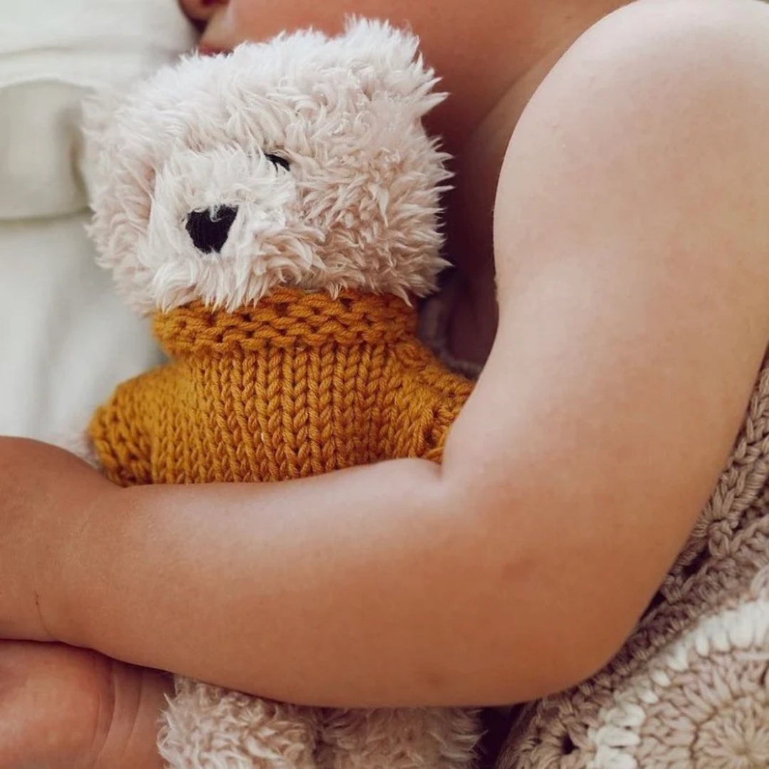 Close-up of a child cuddling a soft cream teddy bear wearing a mustard yellow knitted jumper.