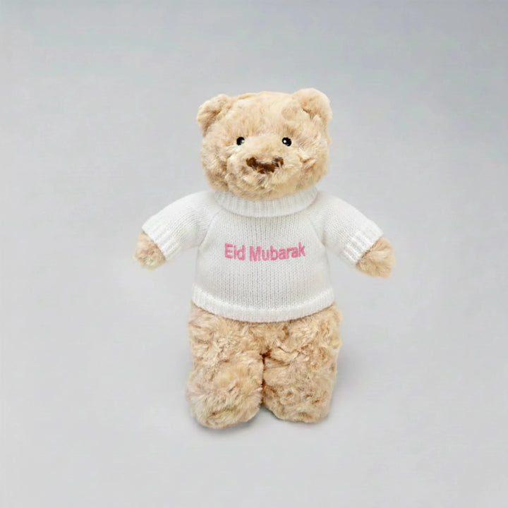 Teddy bear wearing a white sweater with 'Eid Mubarak' text on a gray background