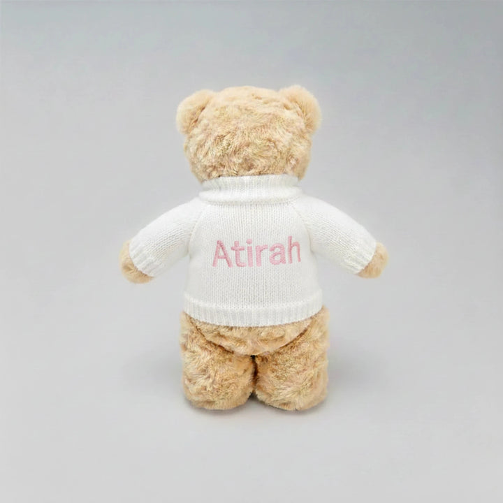 Beige teddy bear wearing a white sweater with 'Atirah' embroidered on a gray background