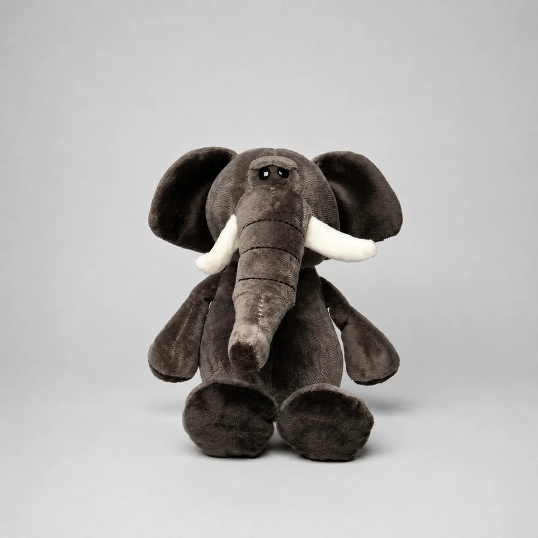 A plush stuffed elephant toy in dark brownish-gray with white tusks, photographed against a plain light gray studio background.