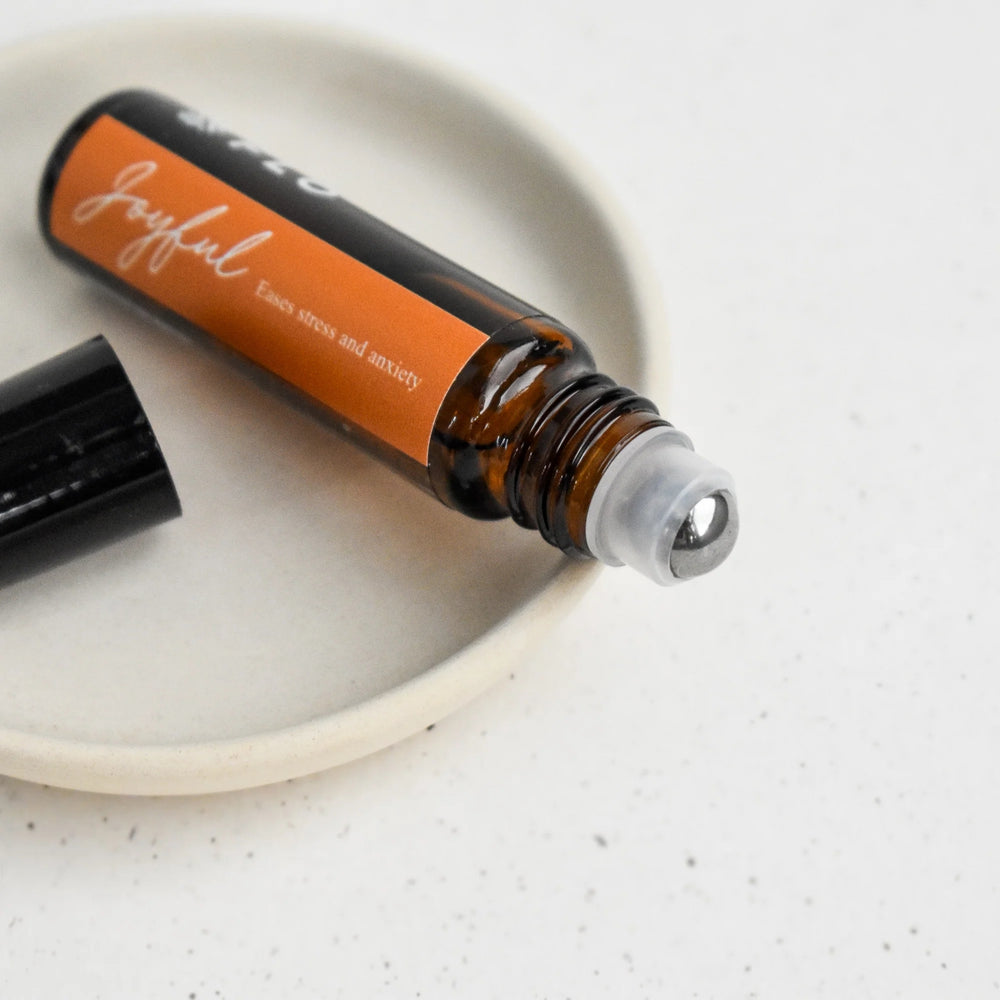 Close-up of Flo Aroma Joyful essential oil roll-on with metal rollerball applicator and orange label reading “Joyful – Eases stress and anxiety.”