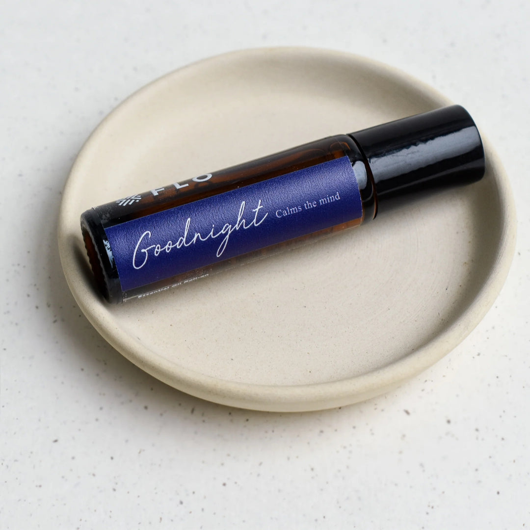 Flo Aroma Goodnight essential oil roll-on resting on a neutral ceramic dish, featuring a purple label that reads “Goodnight – Calms the mind.”