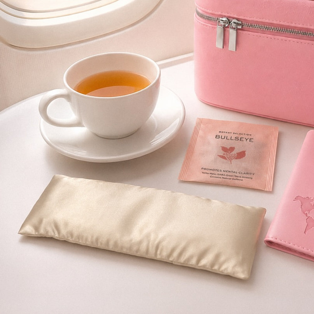 Flo Aroma eye pillow styled for travel beside a cup of tea, pink travel accessories and a botanical sachet.