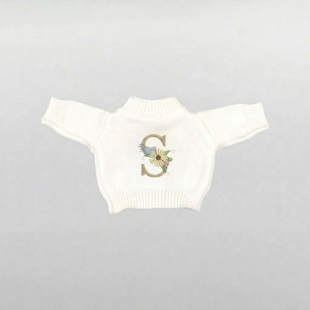 cream soft toy jumper with a decorative flower 'S' on a gray background