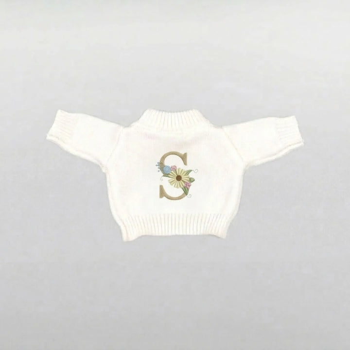 cream soft toy jumper with a decorative flower 'S' on a gray background