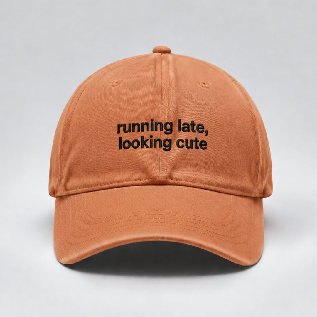 Ginger orange baseball cap embroidered with “running late, looking cute” in black thread across two lines, featuring a curved brim and minimalist design.