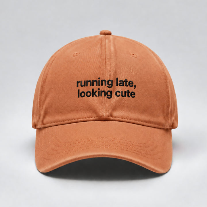 Ginger orange baseball cap embroidered with “running late, looking cute” in black thread across two lines, featuring a curved brim and minimalist design.