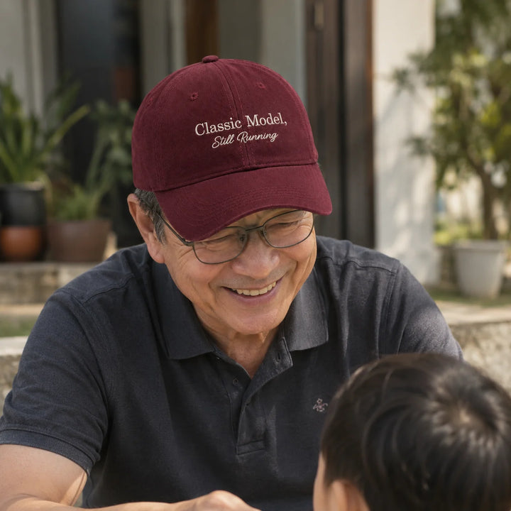 Asian grandfather wearing a personalised “Classic Model, Still Running” cap while smiling at his grandchild outdoors.
