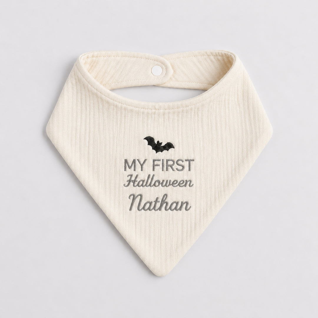 Personalised cream baby bandana bib with a black embroidered bat, grey “My First Halloween” design and the name Nathan.