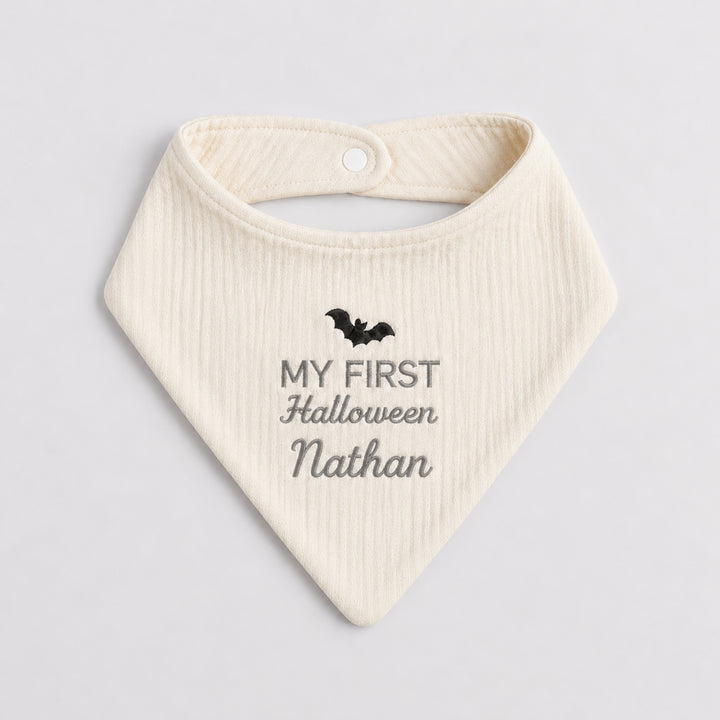 Personalised cream baby bandana bib with a black embroidered bat, grey “My First Halloween” design and the name Nathan.